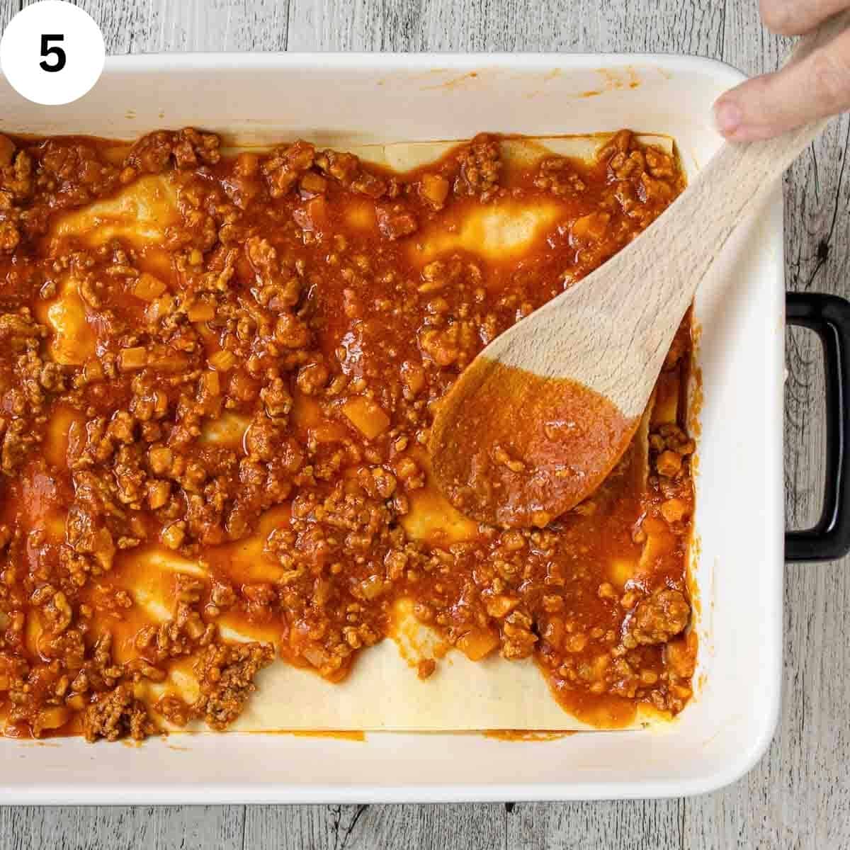 Meat sauce being spread over pasta sheets.