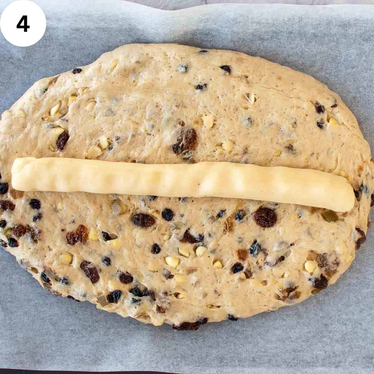 Dough with dried fruit through it, in a flat oval shape with a long log of marzipan on top.