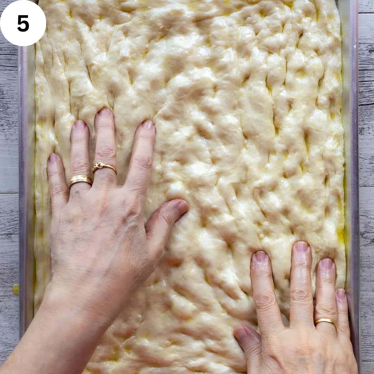 Fingers pressing out pizza dough into a rectangle pan.