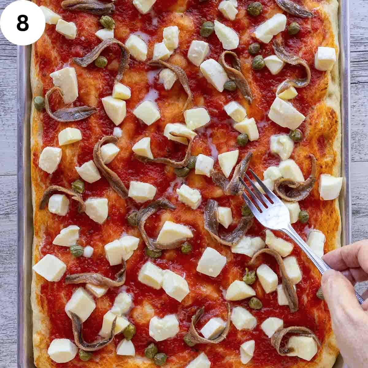 Arranging anchovies on a pizza base in a rectangle pan.