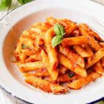 Penne Pomodoro in a bowl garnished with a sprig of basil leaves.