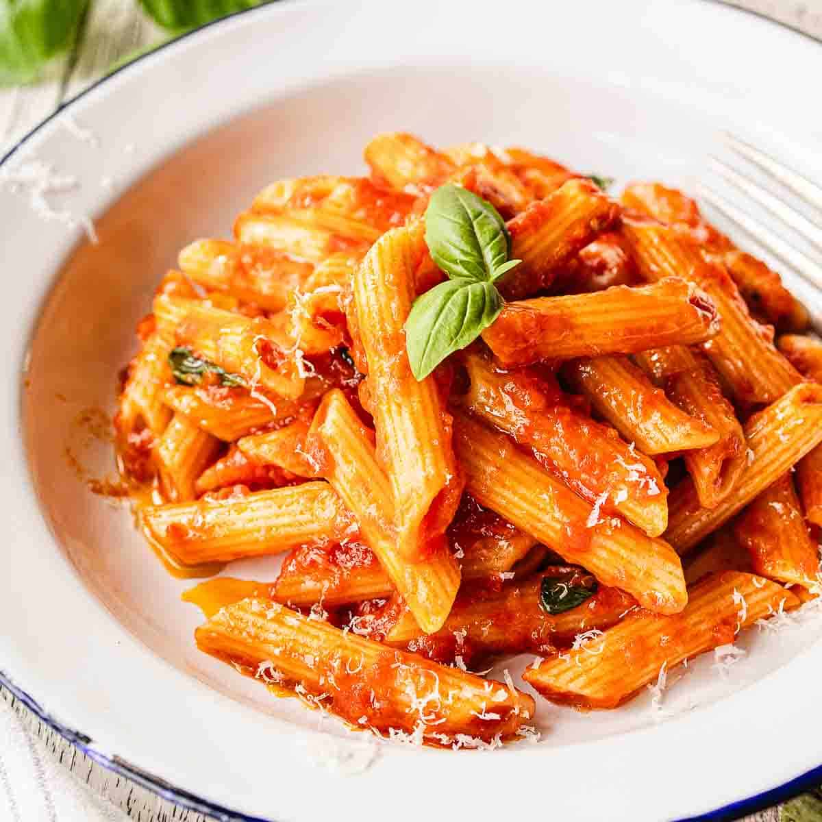 Penne Pomodoro in a bowl garnished with a sprig of basil leaves.