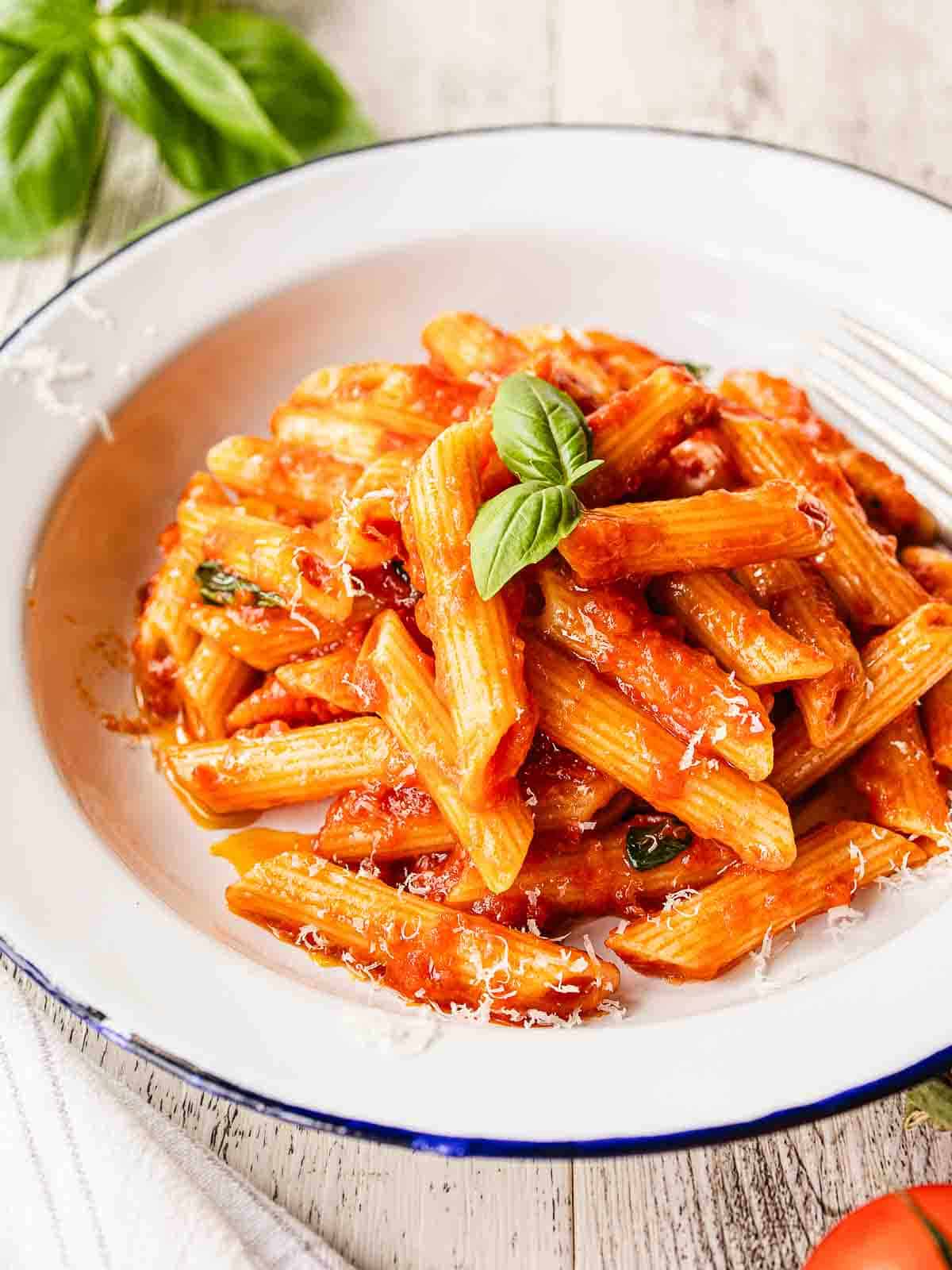 Penne Pomodoro in a bowl garnished with a sprig of basil leaves.
