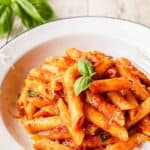 Penne Pomodoro in a bowl garnished with a sprig of basil leaves.