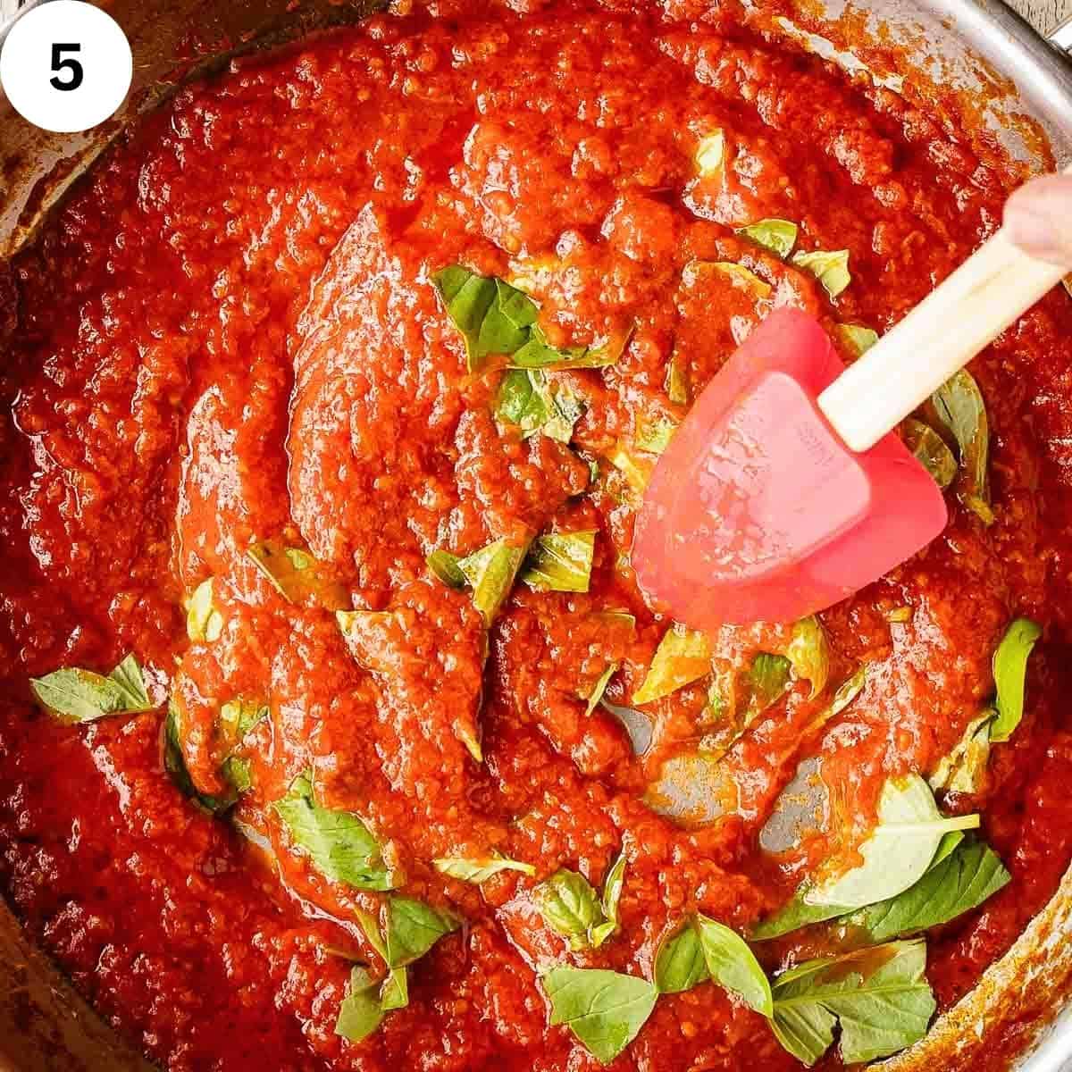 Stirring chopped fresh basil through tomato pasta sauce.