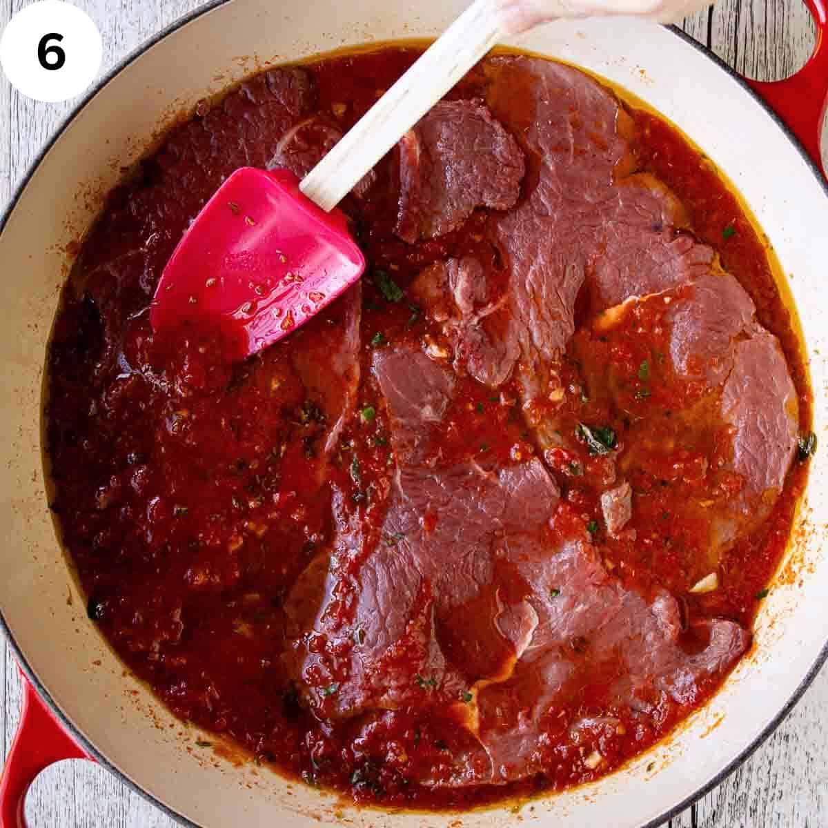 Spooning tomato puree onto steaks in a pan.