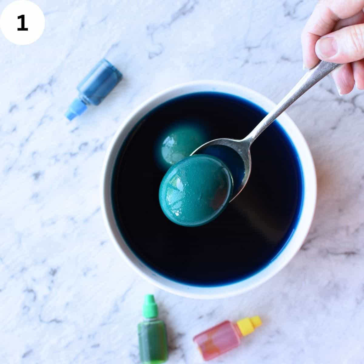 Raw egg in the shell being dipped into food coloring.