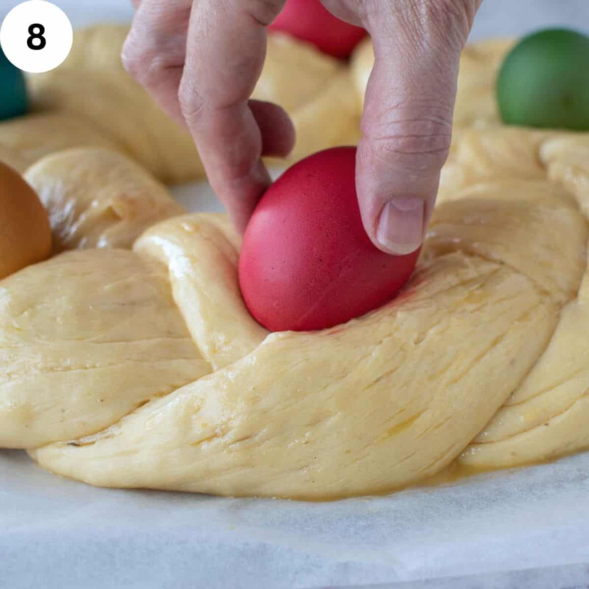 Placing a colored egg onto uncooked braided dough.