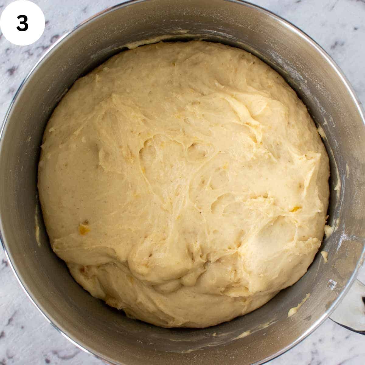 Dough in a stainless steel bowl with a scraggy surface.