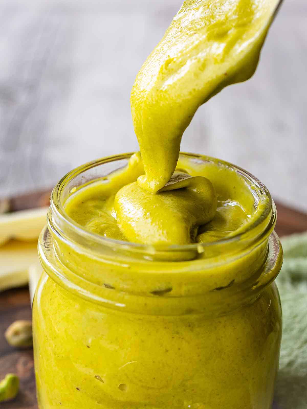 A pistachio cream recipe prepared and being spooned into a glass jar.