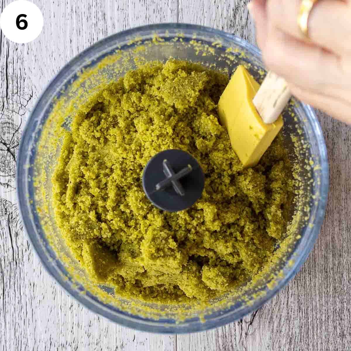 Scraping the sides of a food processor containing ground pistachios.
