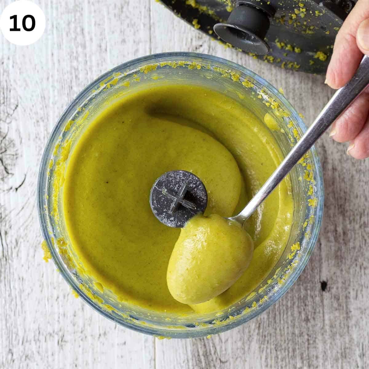 A spoon scooping up homemade pistachio cream from food processor.