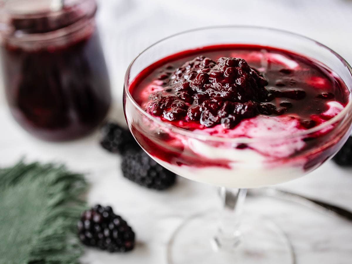 A berry sauce partially mixed through plain yogurt in a shallow glass.