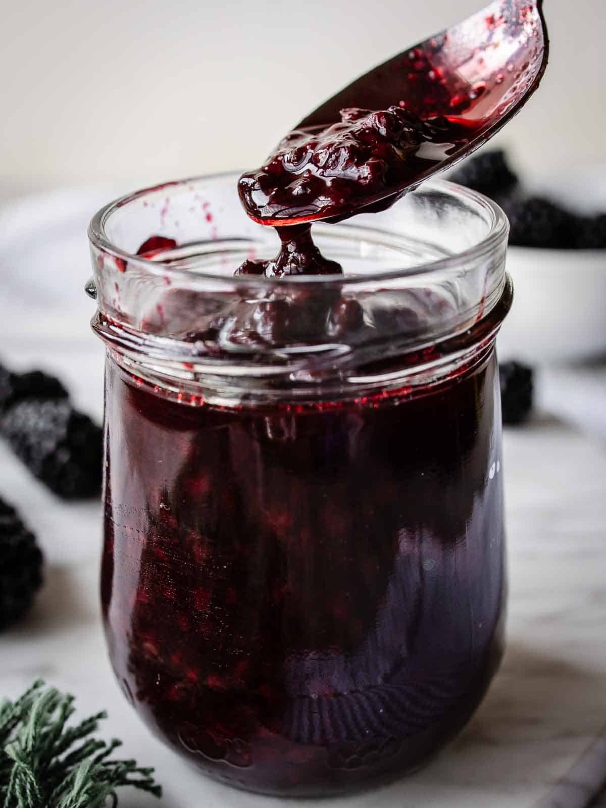 Blackberry compote being spooned into a glass jar.
