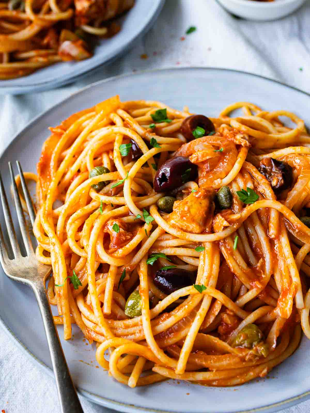 Plate of the tuna pasta recipe consisting of spaghetti in tomato sauce, with olives and chopped parsley.