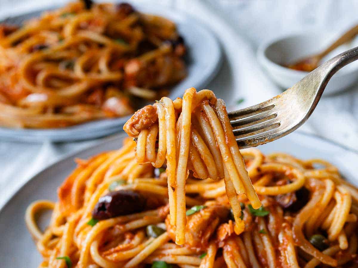 Tuna Spaghetti twisted around a fork above a plate of spaghetti.
