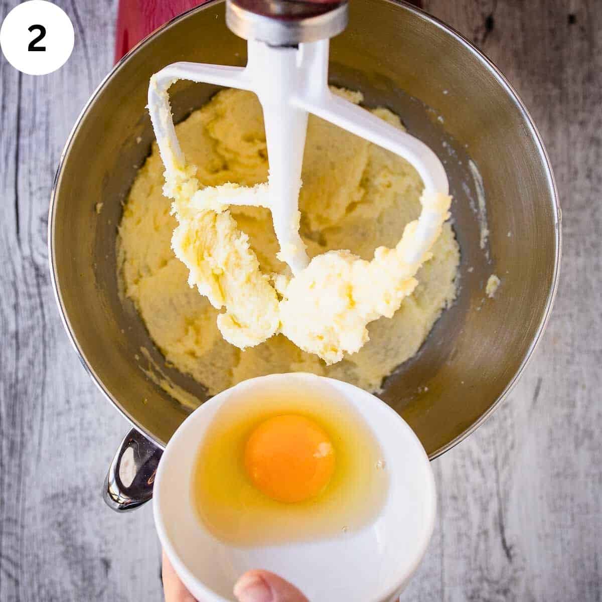 A hand mixing an egg into a bowl of butter and sugar.