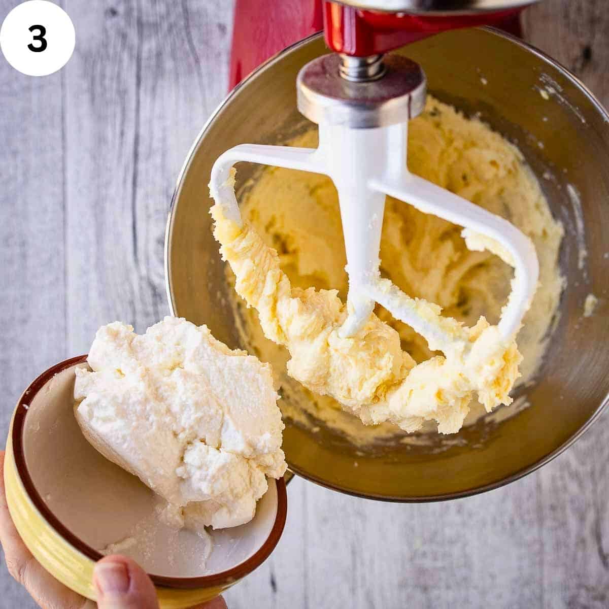 A hand holding a bowl of ricotta which is being added to batter.
