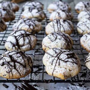 Chocolate drizzled cannoli cookies on a cooling rack.