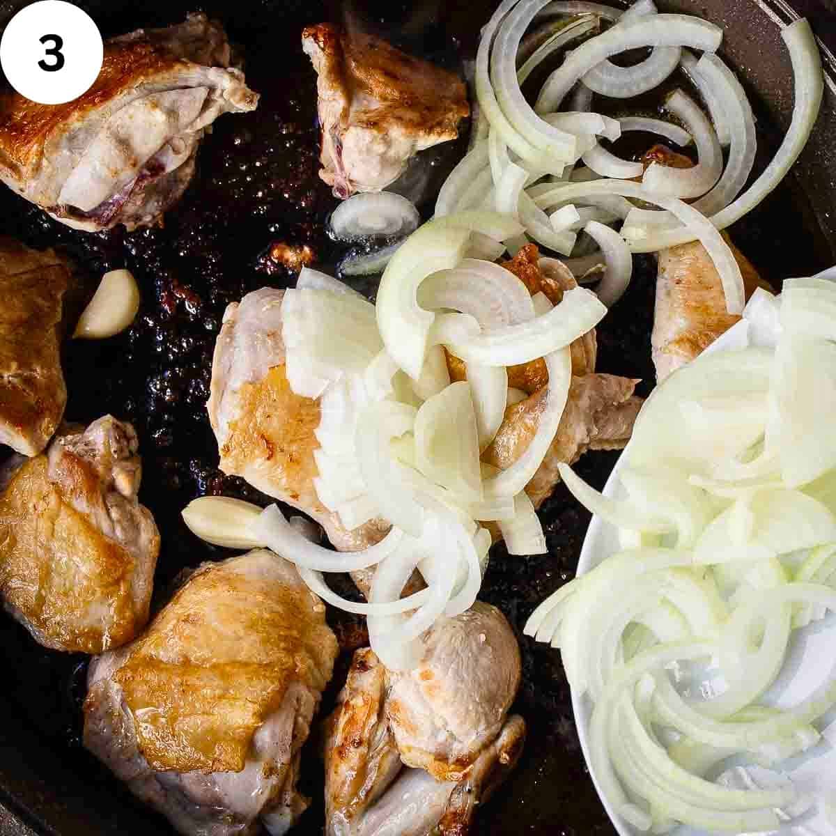 Sliced onion being added to fried chicken in a pan.