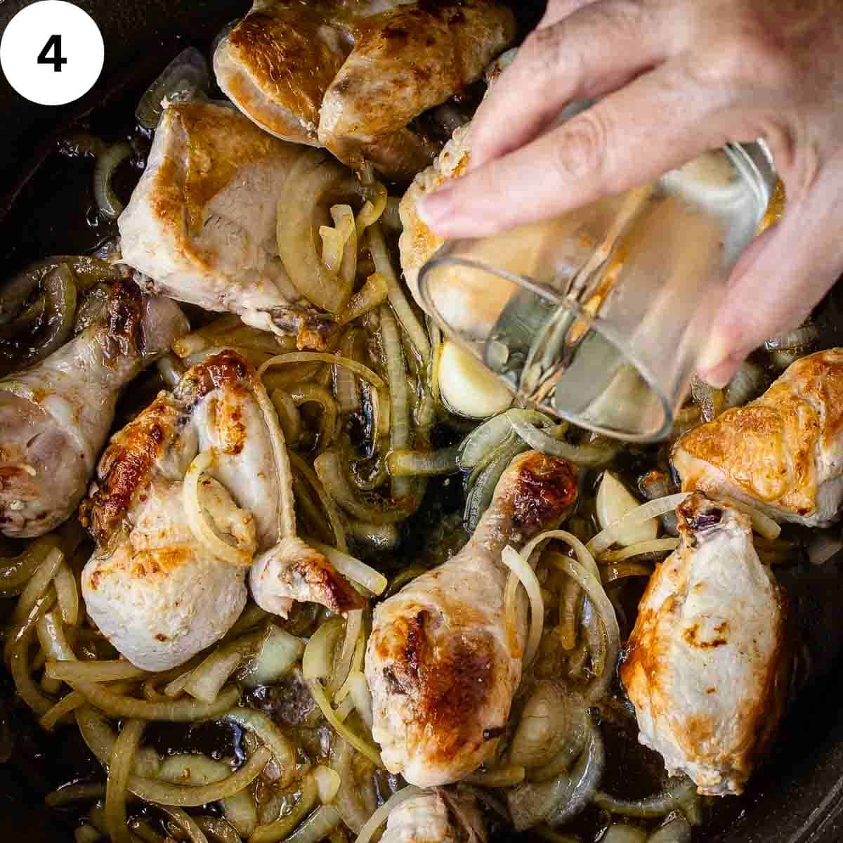 A person adding white wine to fried chicken and onions in a pan.