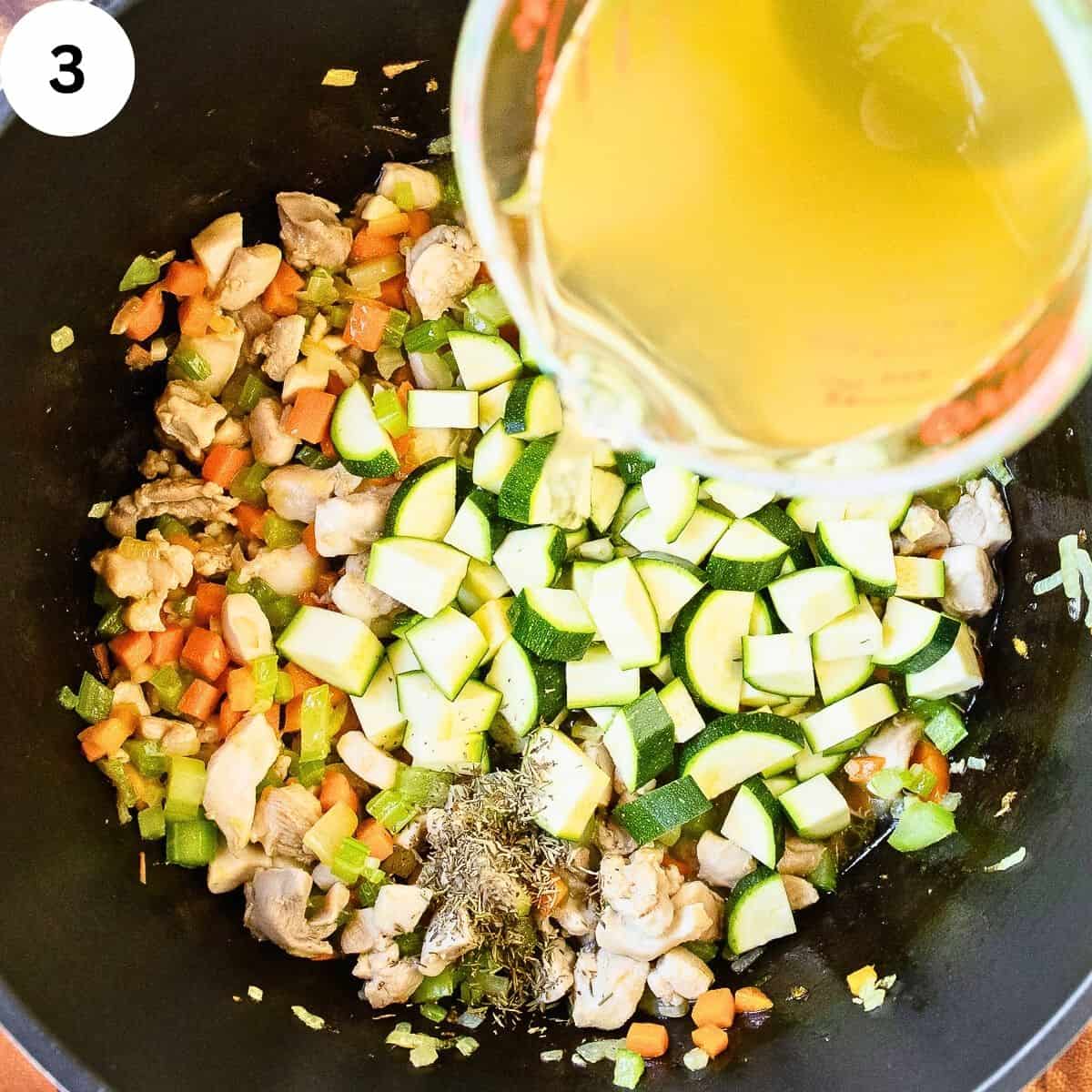 Pouring chicken broth into vegetables in a saucepan.