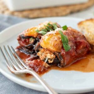 Close up of two eggplant involtini on a white plate.