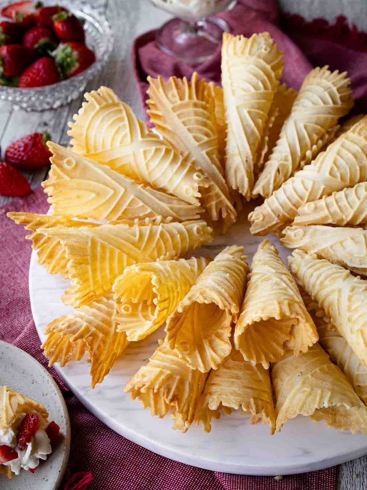 A plate of krumkake with strawberries around it.