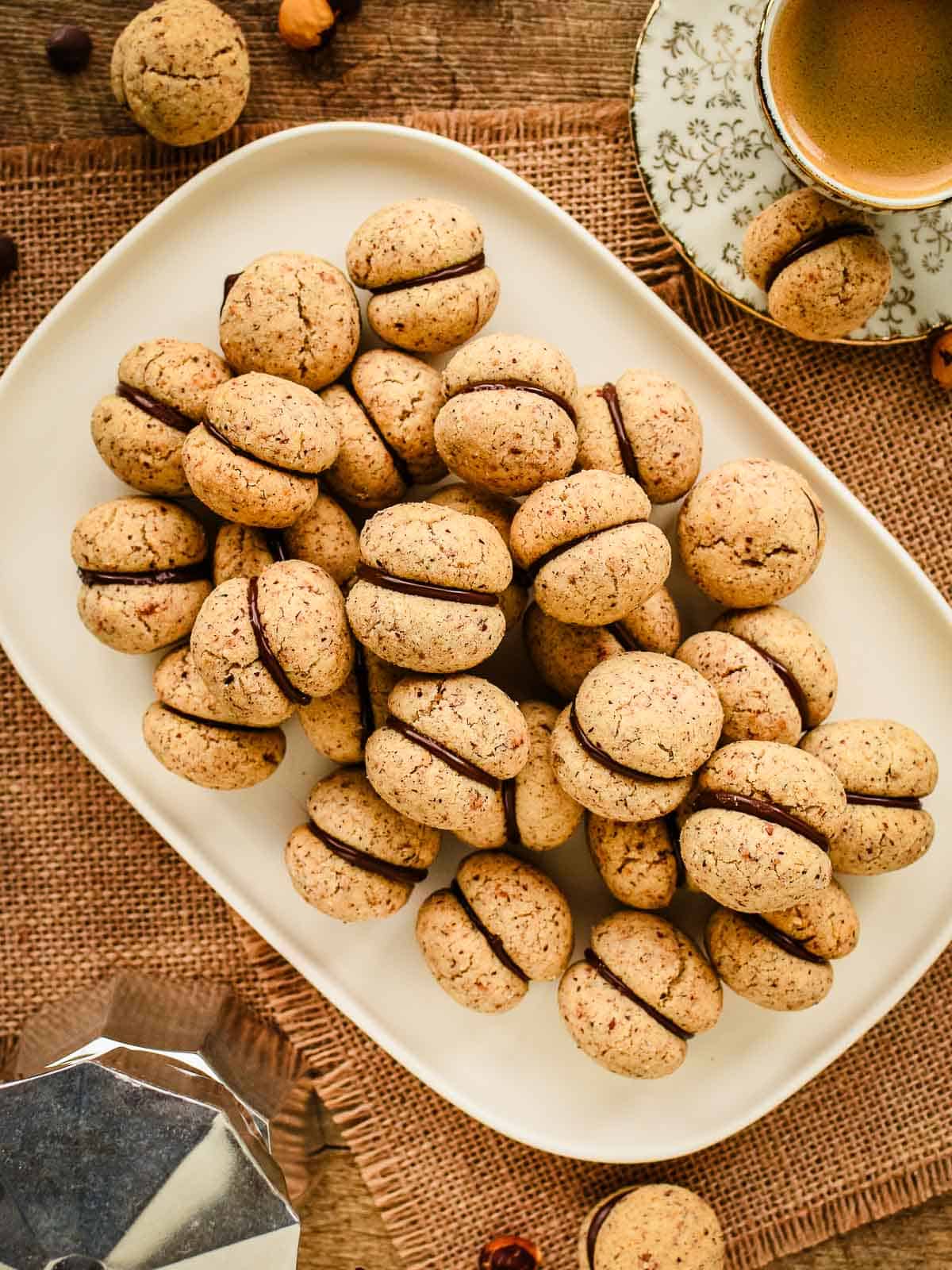 Overhead view of hazelnut sandwich cookies filled with chocolate piled on a oblong plate.