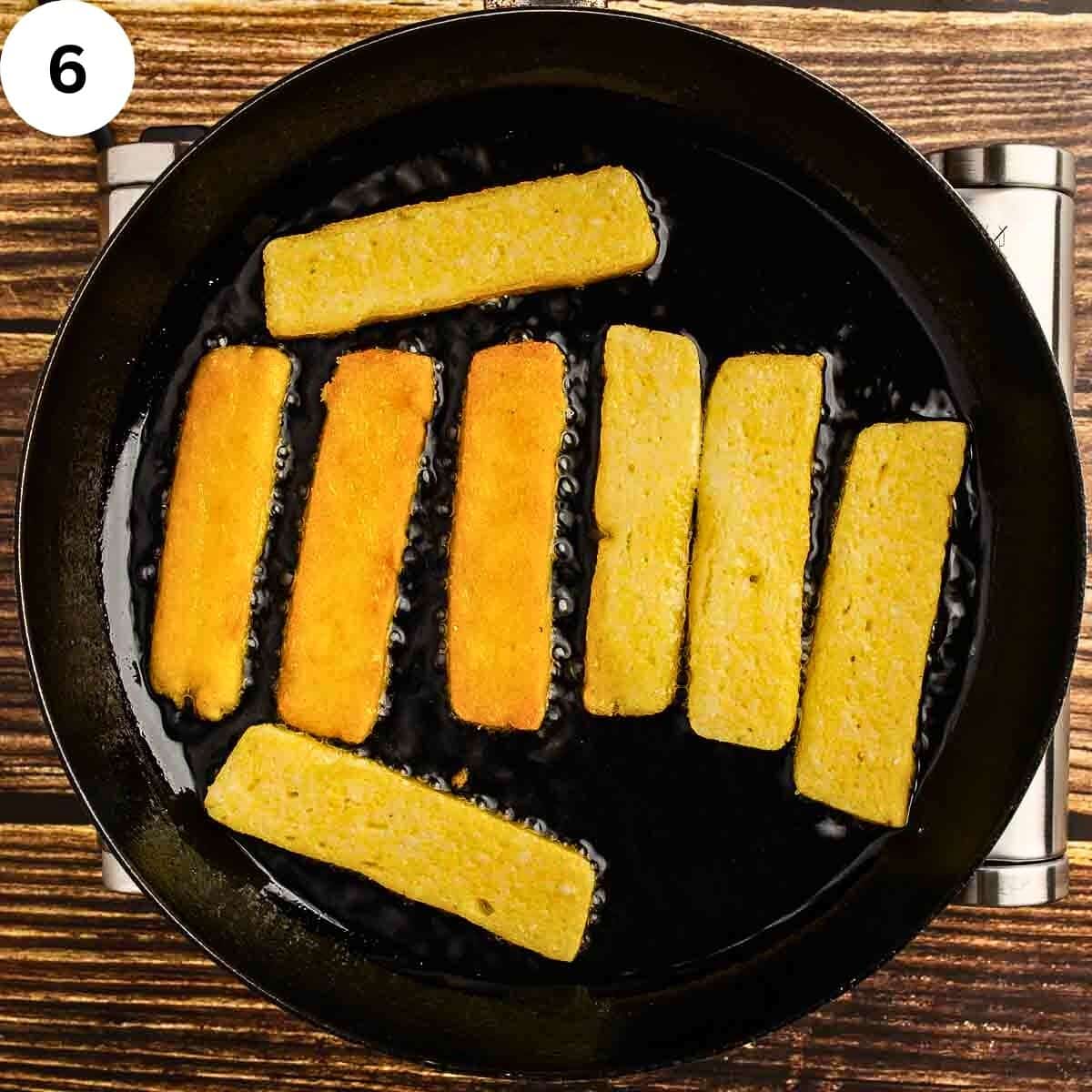 Stick of polenta frying olive oil in a skillet.
