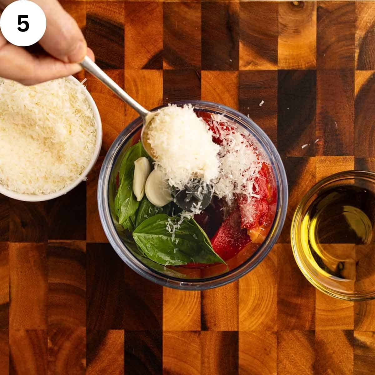 Spooning grated Parmesan cheese into a blender with other ingredients.