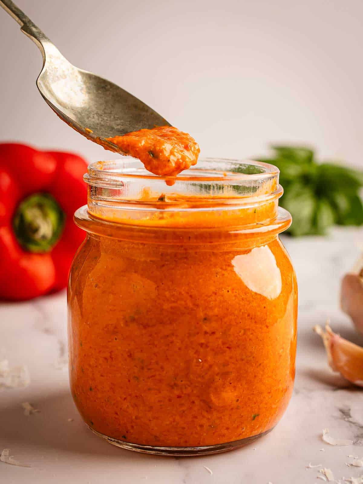 Jar of roasted red pepper sauce with a spoon taking a scoop.