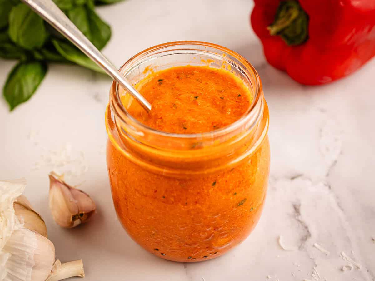 A jar of cream bell pepper sauce with a spoon in it.
