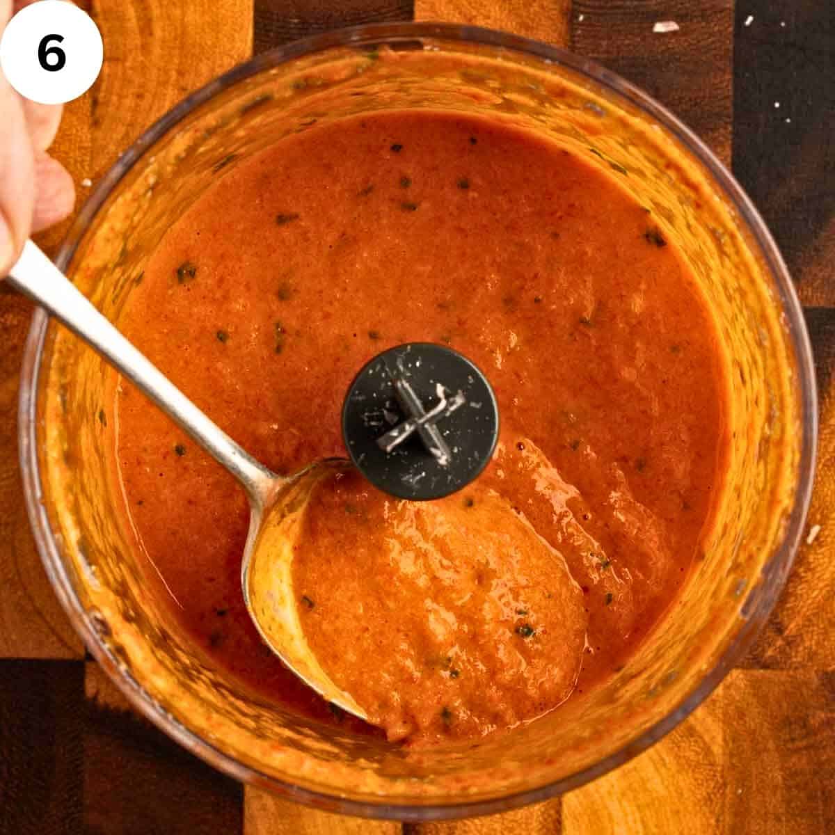 Roasted bell pepper sauce in a food processor with a spoon scooping some out.