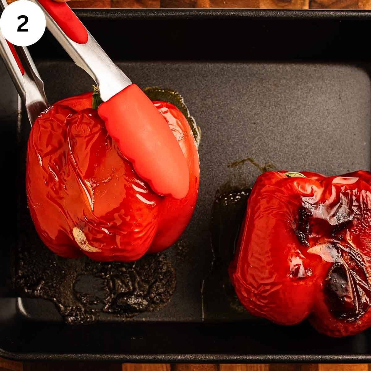 Two red roasted red peppers; one being picked up with tongs.