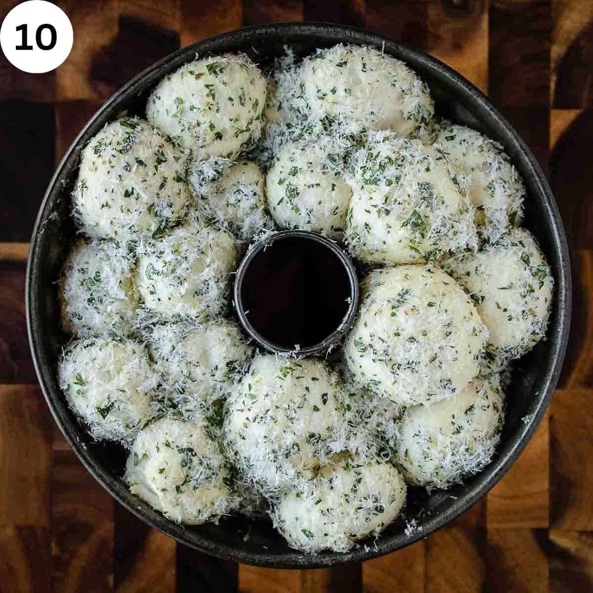 Risen bread dough balls coated in Parmesan cheese and herbs in a bundt pan.