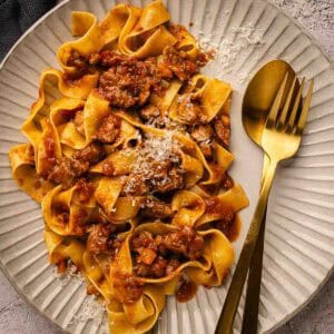 Overhead view of pappardelle pasta with pork ragu sauce on a plate with fork and spoon.