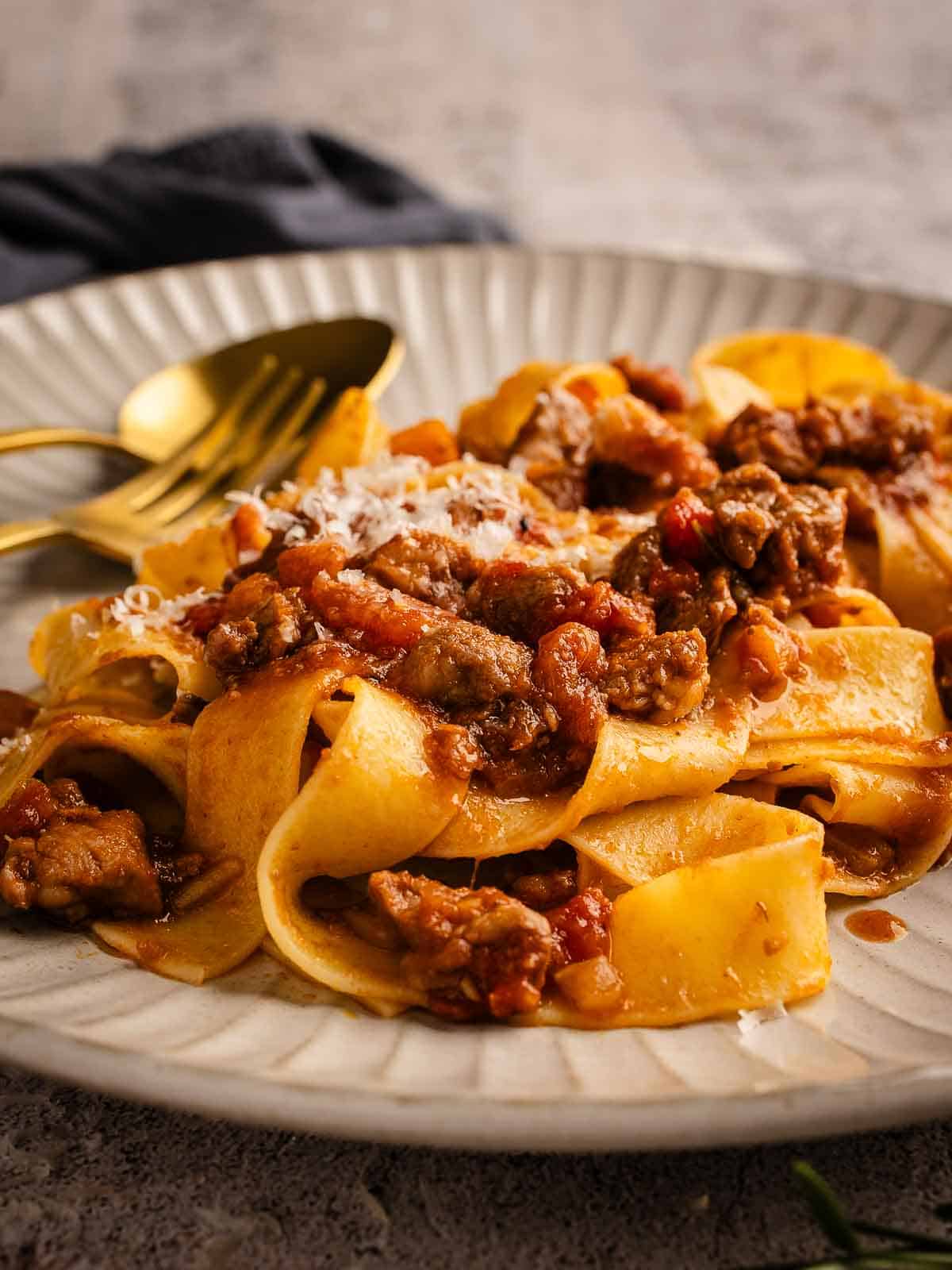 Pork ragu sauce on pappardelle pasta on a plate with fork and spoon.