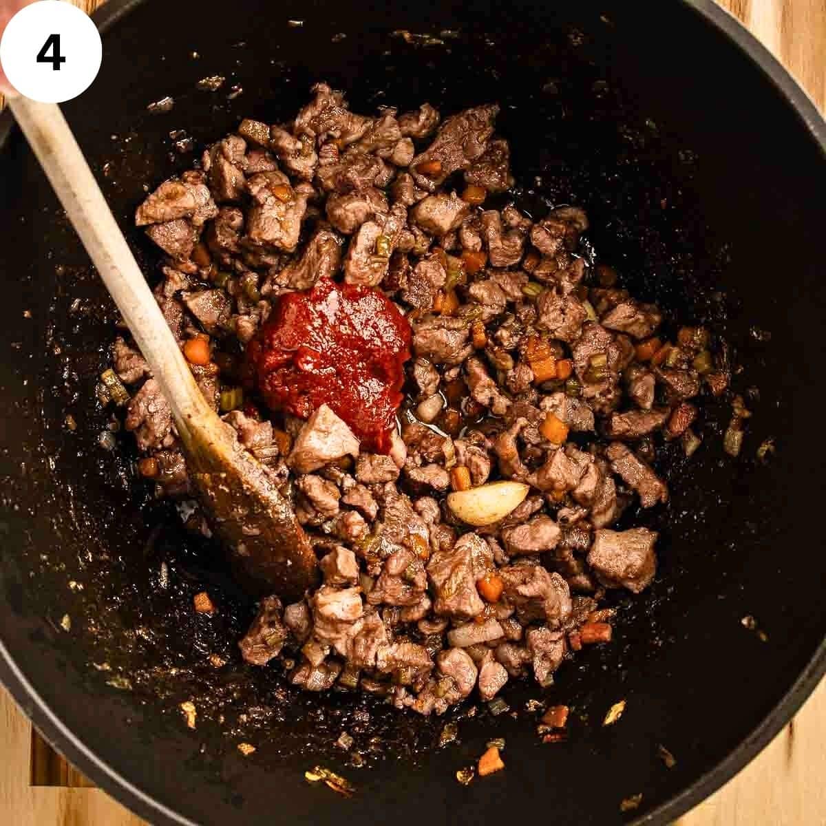 Stirring tomato paste into cooked, chopped meat in a saucepan.