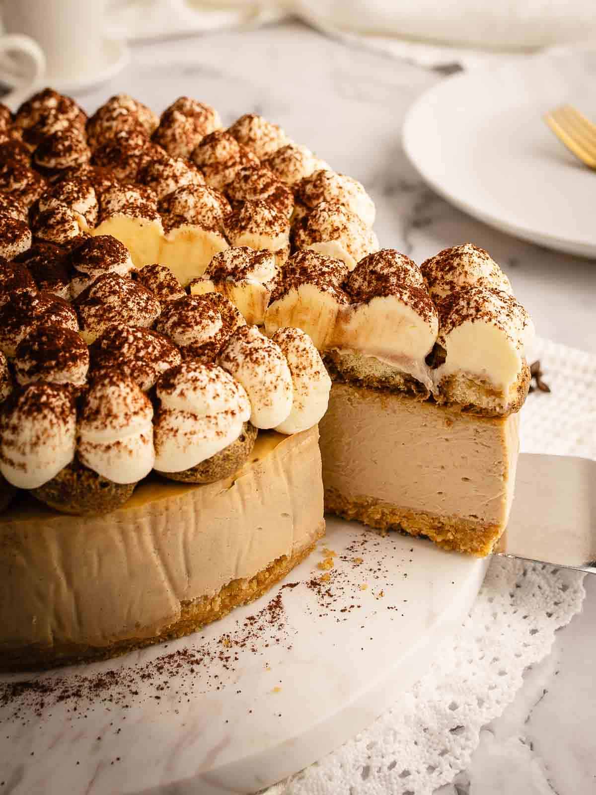 Baked tiramisu cheesecake with a slice cut and being removed on a cake server.