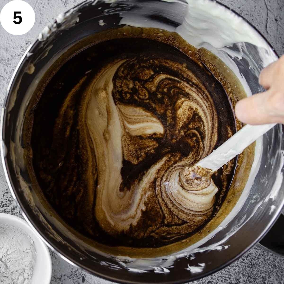 Mixing dark liquid into a creamy mixture with a spatula.
