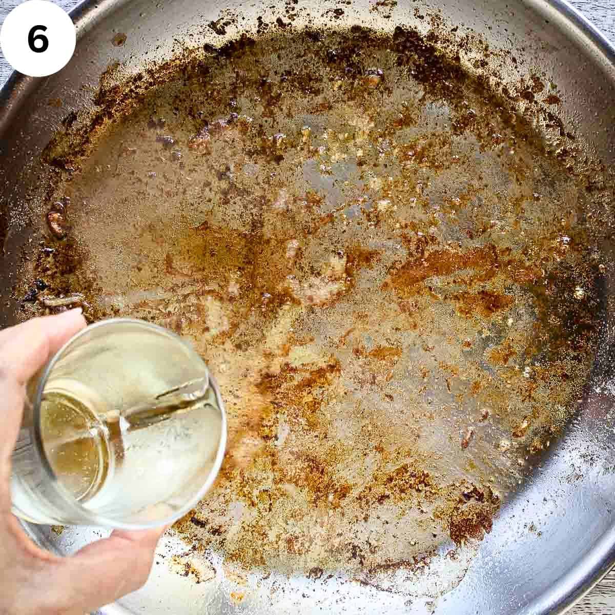 Pouring white wine into a pan which has been used to fry and has browned bits.