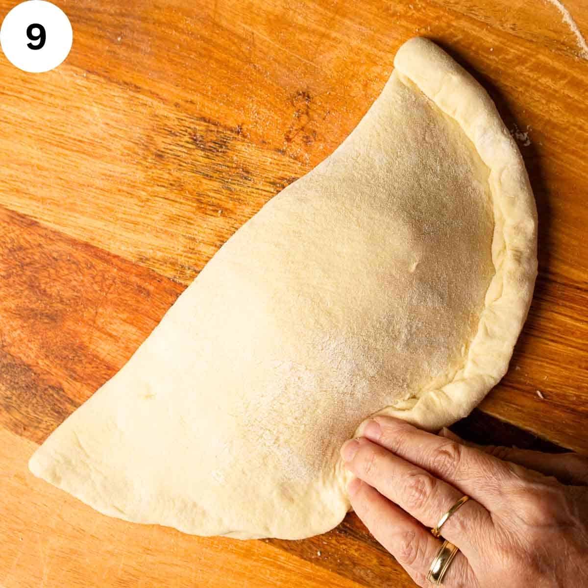 Pinching the edges of folded dough to seal a calzone before baking.