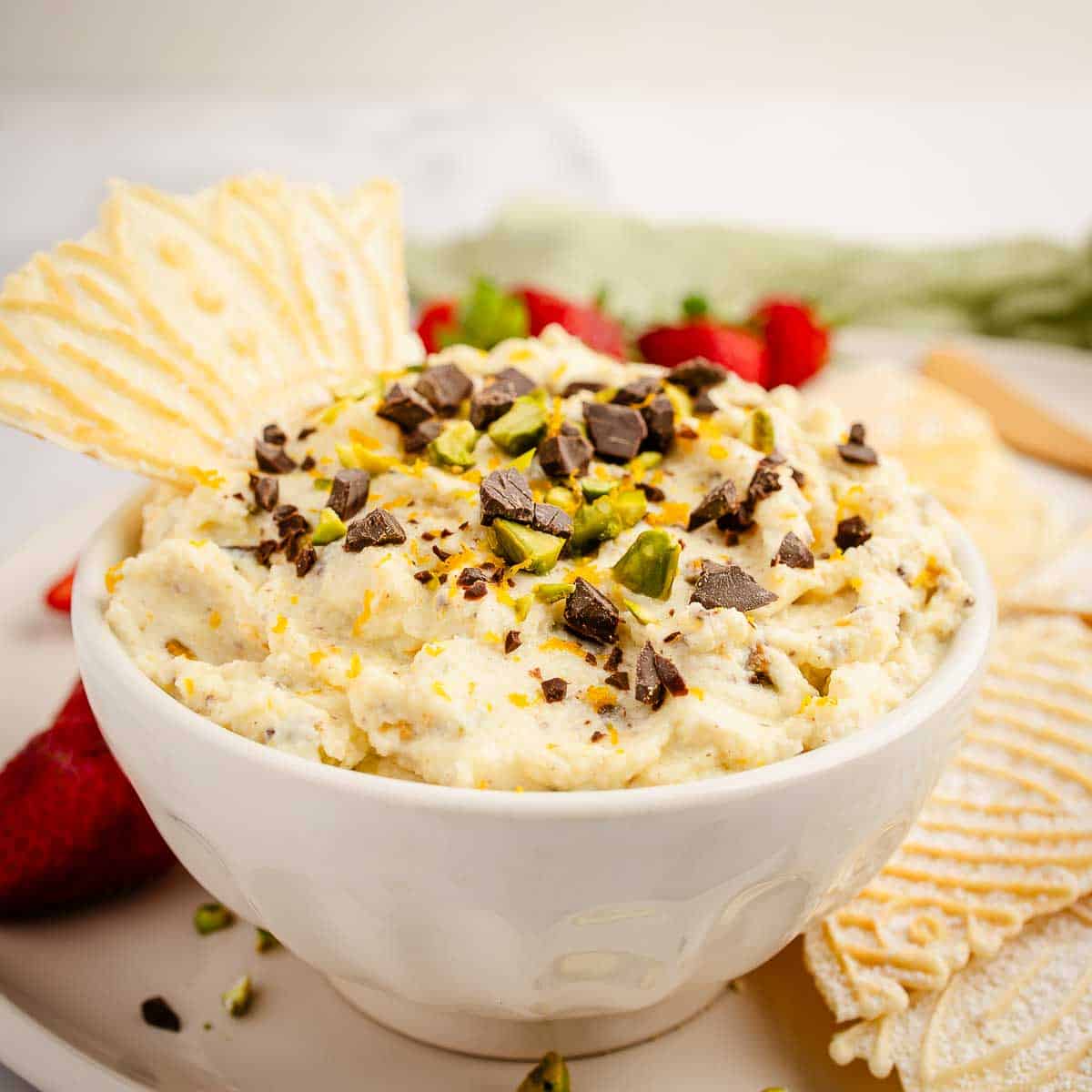 Creamy cannoli dip topped with chocolate chips and chopped pistachios and served with crispy pizzelle.