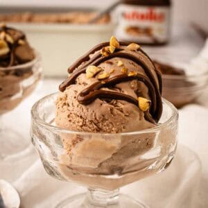 Scoop of Nutella ice cream in a dessert glass topped with drizzled Nutella and chopped hazelnuts