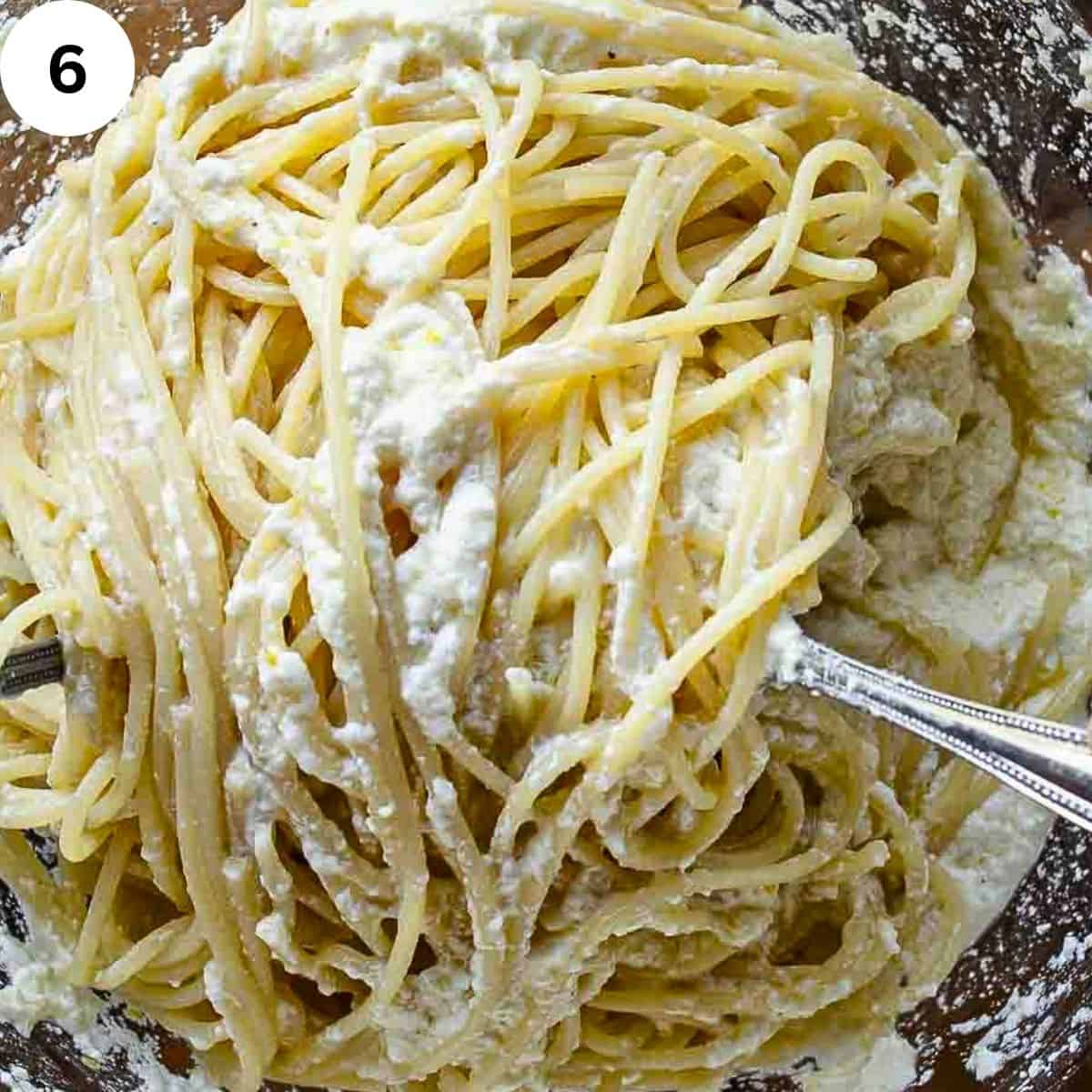 Mixing cooked spaghetti with lemon ricotta sauce.