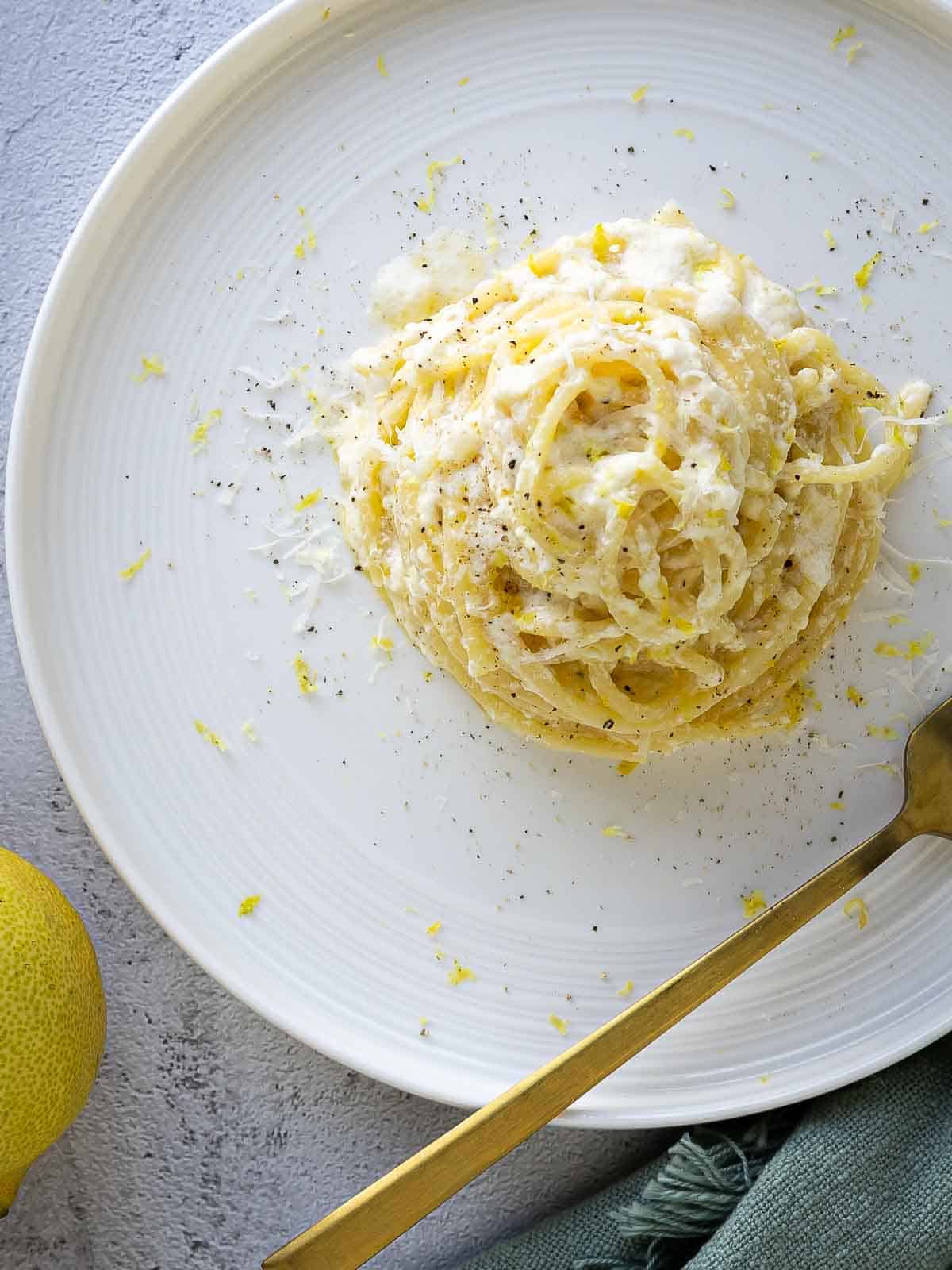 Overhead view of pasta with lemon ricotta sauce on a round plate with a fork.