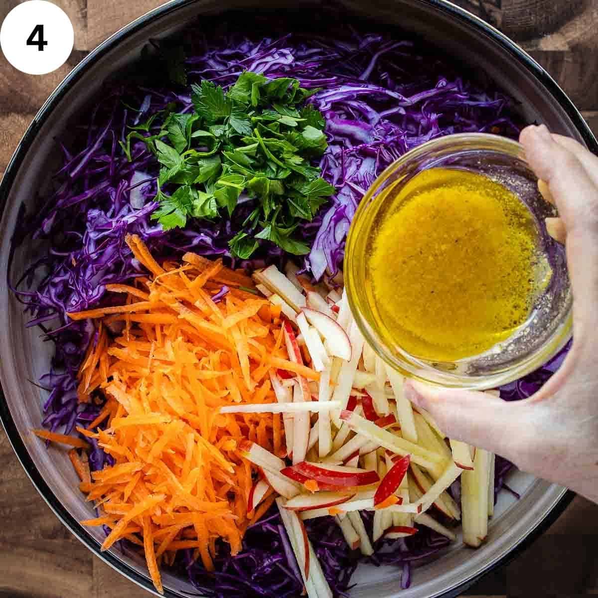 Pouring dressing onto a salad of red cabbage, carrot, and apple.