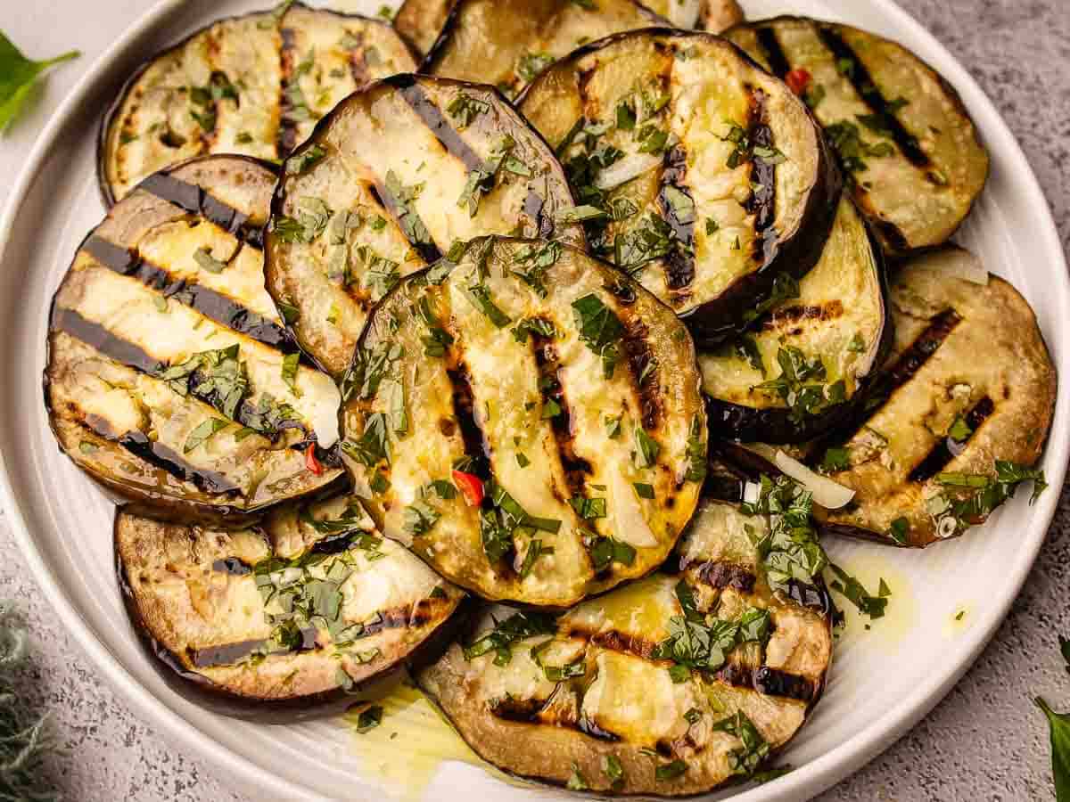 Sliced eggplant with grill marks from cooking piled onto a round plate.