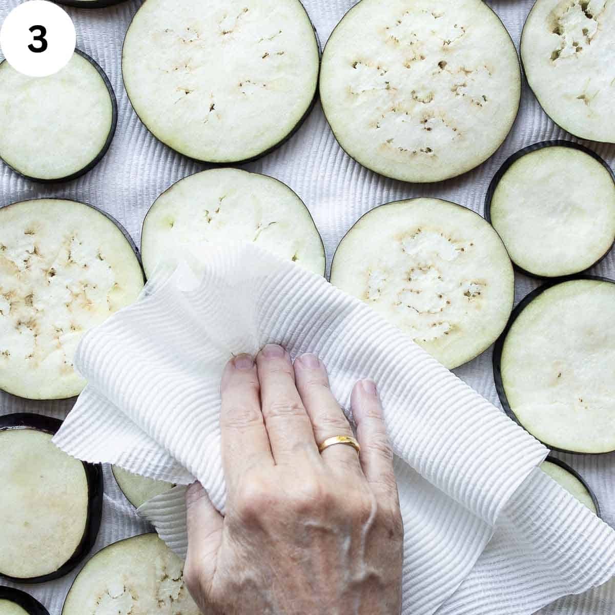 Patting the eggplant slices dry with a paper towel.